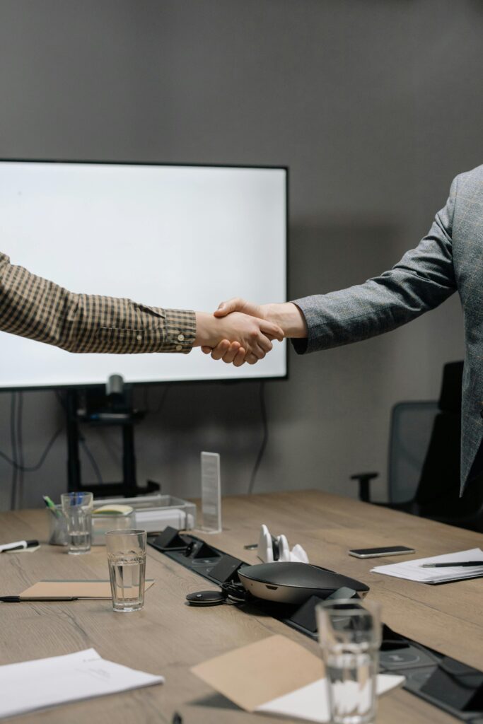 Two business professionals shaking hands in a modern meeting room, symbolizing successful collaboration.